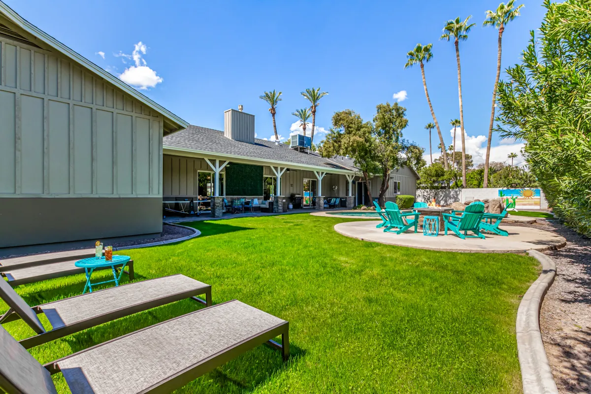 A broad view of the poolside area, featuring ample lawn space, sun loungers, and Adirondack chairs arranged for socializing or soaking up the sun. The pathway guides guests through the manicured backyard, reinforcing the sense of space and privacy.