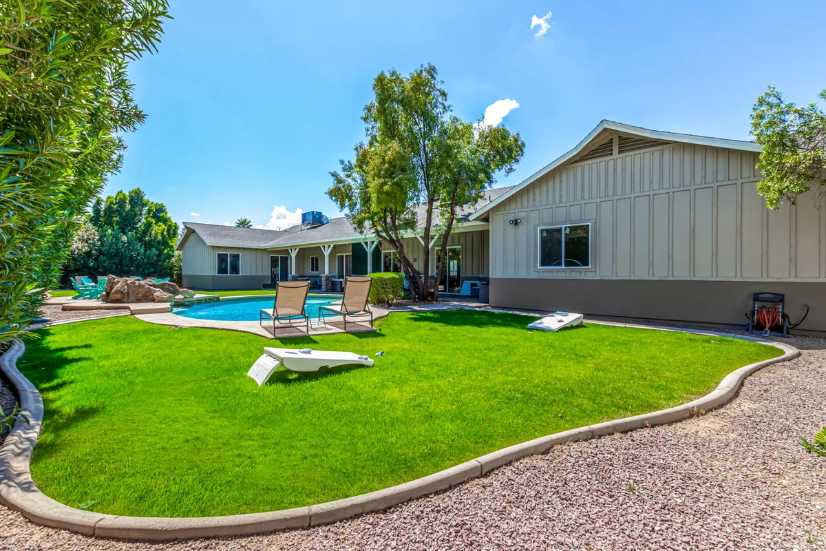 A vibrant exterior scene showcasing a sparkling pool surrounded by a lush green lawn and several outdoor lounge chairs. The backdrop includes the home’s exterior, suggesting both privacy and luxurious relaxation. The setting is sunlit, evoking an inviting, resort-style atmosphere ideal for unwinding after a workday or hosting casual corporate gatherings.