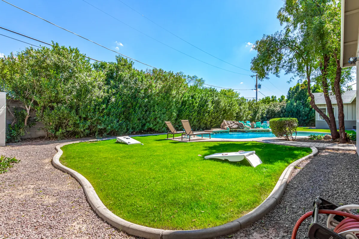 An inviting backyard scene featuring a private swimming pool, lounge chairs, green lawn, and hedges. The cheerful setup highlights a safe, private space for families to unwind and play together after a day of exploring.