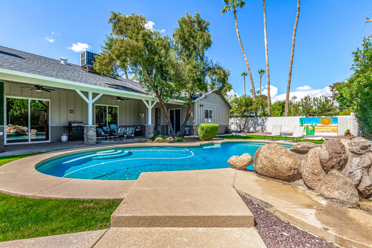 An inviting exterior view of a swimming pool framed by a landscaped garden and comfortable outdoor seating. Rock features and greenery add to the resort-style ambiance, while the arrangement suggests ample space for informal meetings, team-building, or socializing outdoors.