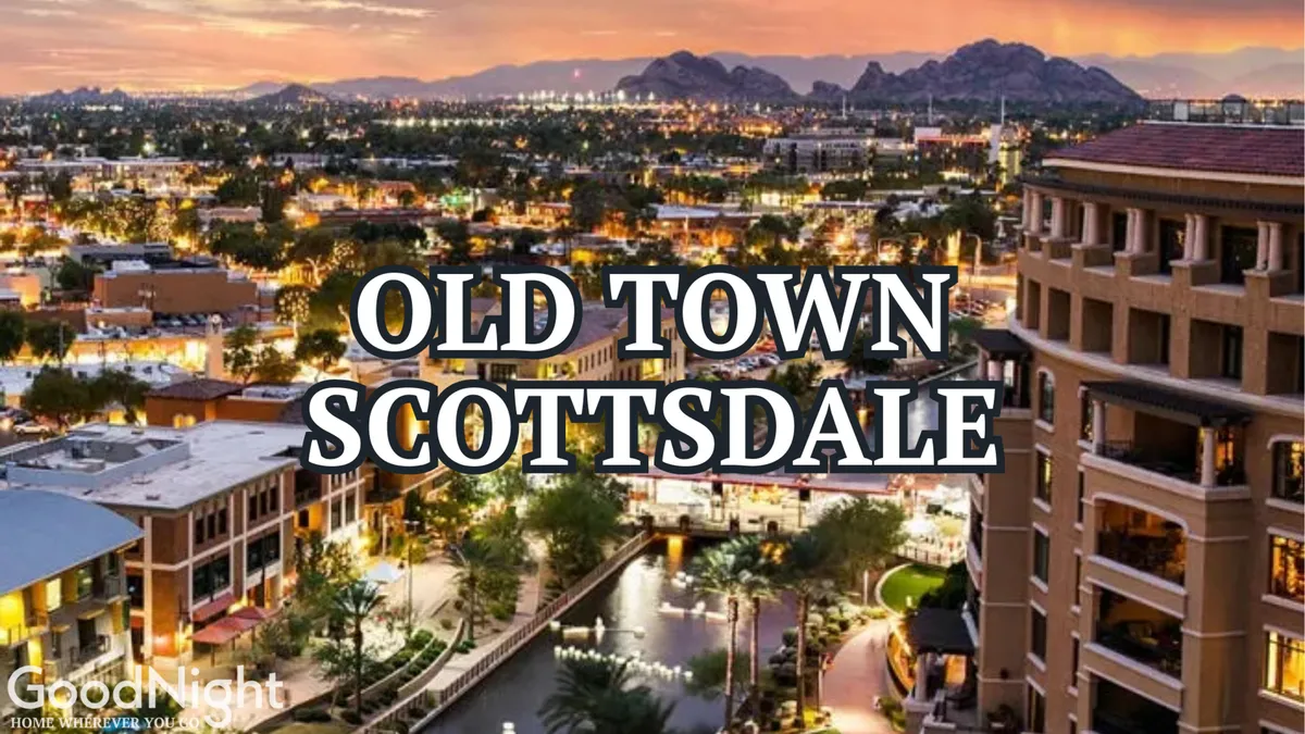 A vibrant view of Old Town Scottsdale featuring illuminated buildings, palm trees, and mountains in the distance, with lively activity along the promenade, outdoor cafes, and water features reflecting the city lights.