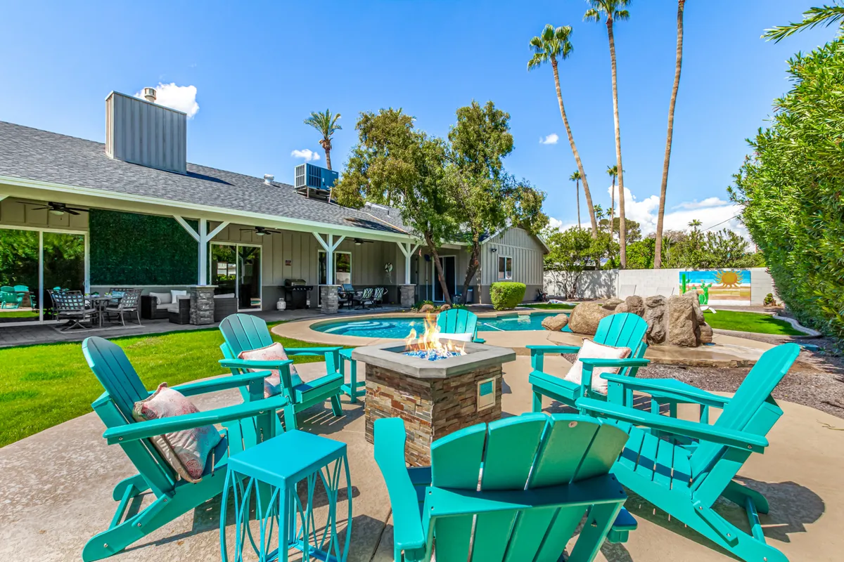 This image spotlights a vibrant backyard scene featuring a sparkling swimming pool, inviting lounge chairs, a stylish gas fire pit, and lush landscaping. The layout is ideal for both sunbathing and social gatherings, with the fire pit set up as a focal point for evening relaxation.