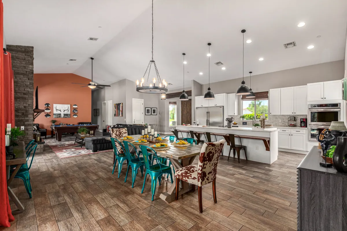 The dining area is shown with a spacious table set for eight, surrounded by colorful chairs, adjacent to the kitchen island and visible pool table. Decorative wall art and modern lighting complement the lively atmosphere, emphasizing spaces perfect for meals and celebrations.