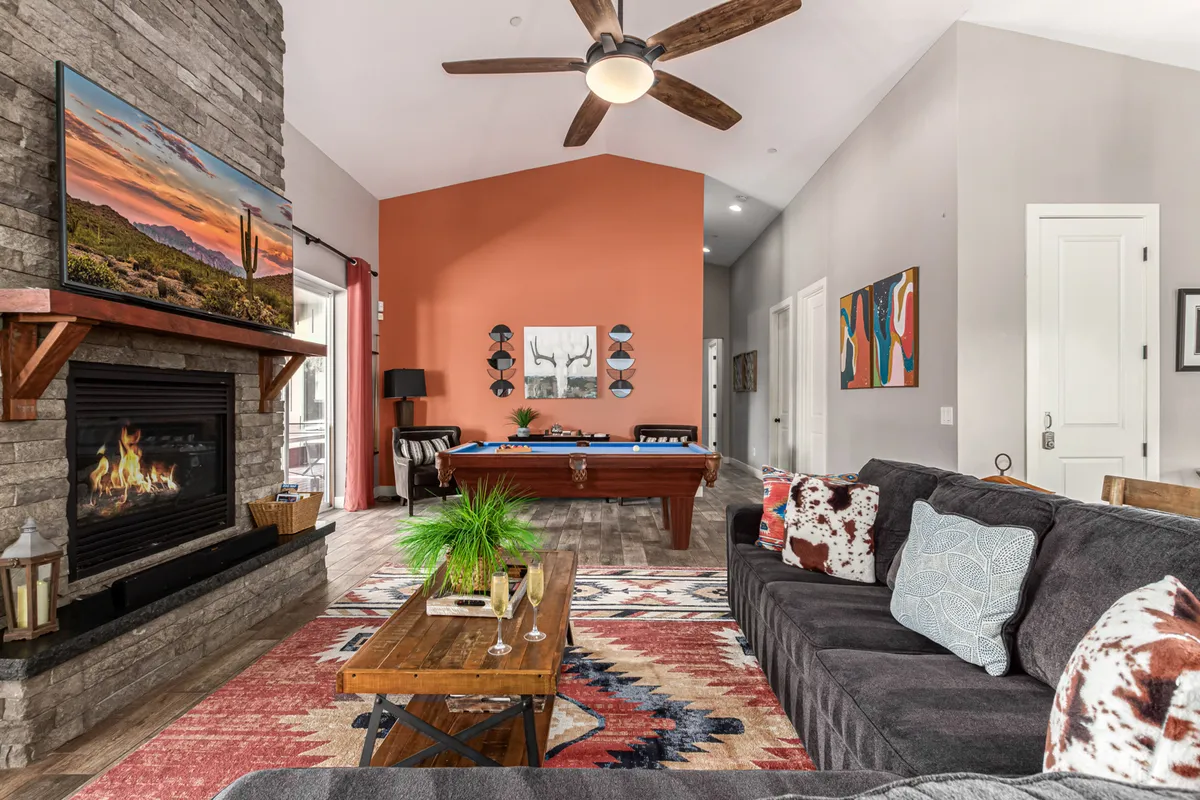 A cozy living room centered around a sleek pool table, with a comfortable sofa seating area and a mounted TV above a modern fireplace. The inviting ambiance encourages both friendly competition and relaxed social gatherings.