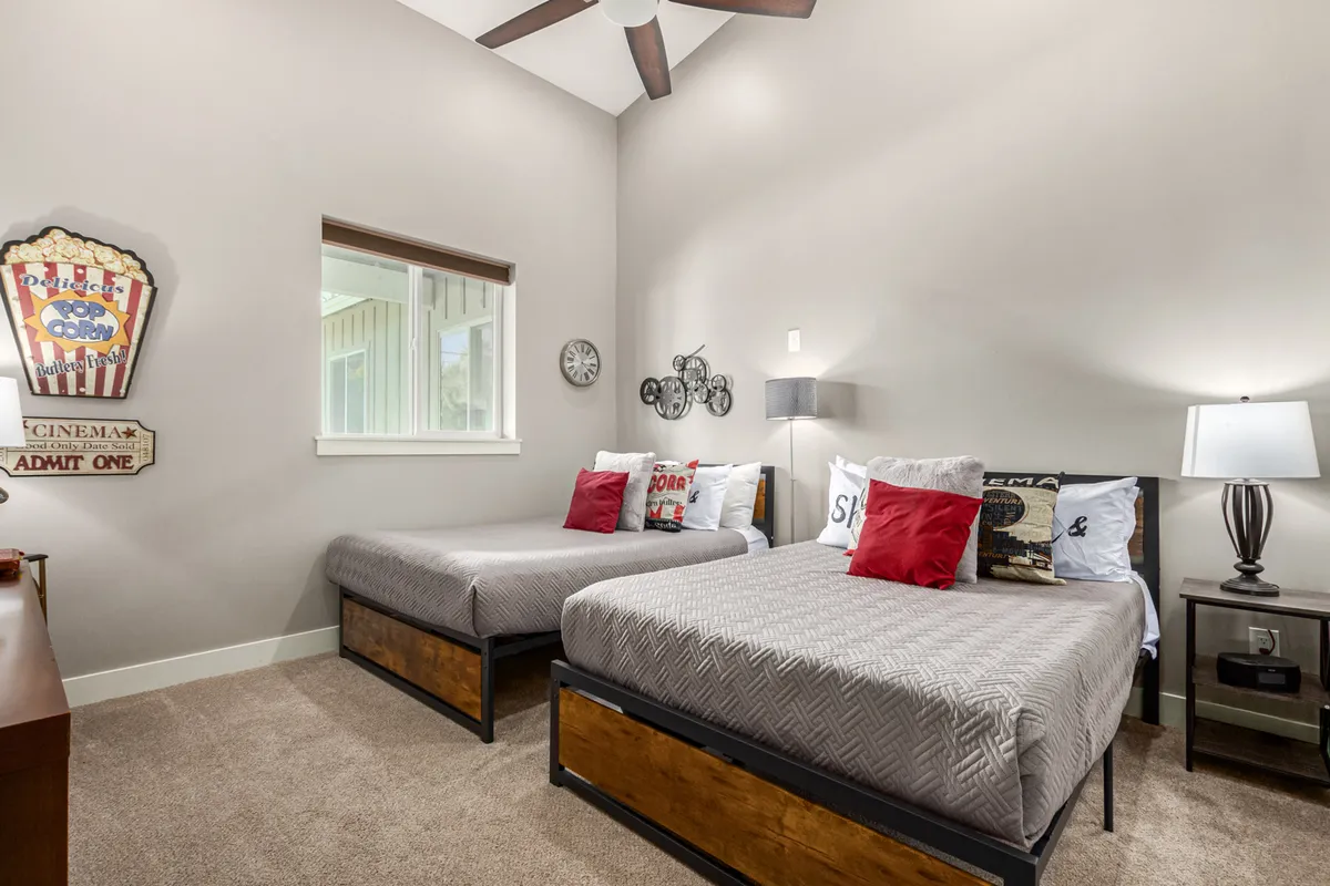 A cozy bedroom with two beds adorned with decorative pillows, a vintage cinema sign above, a decorative clock, and a table lamp. The space feels inviting and playful, with clear nods to a movie theme and an atmosphere suited for socializing or relaxing.