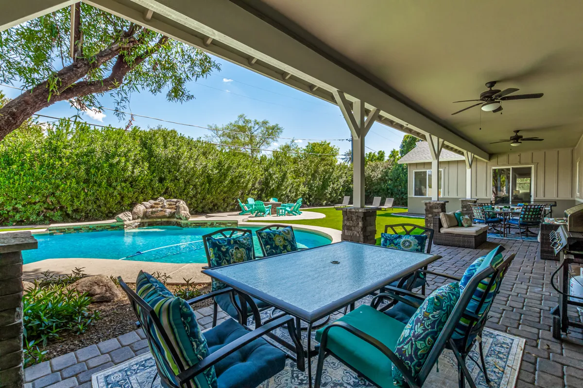 This scene depicts the pool surrounded by an outdoor seating area and lush landscaping, capturing a cheerful, welcoming mood. The layout hints at spaces ideal for dining outdoors, celebrating, or simply unwinding by the water.